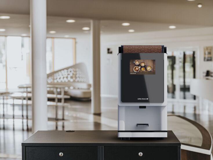 Der weiß lackierte Kaffeevollautomat BARISTA Compact steht auf einem Untertisch im Forum von Kaffee Partner