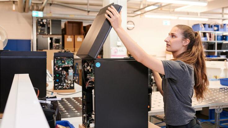 Fachkundige Technikerin klappt einen hochwertigen Kaffeevollautomaten in einer modernen Montagehalle auf.