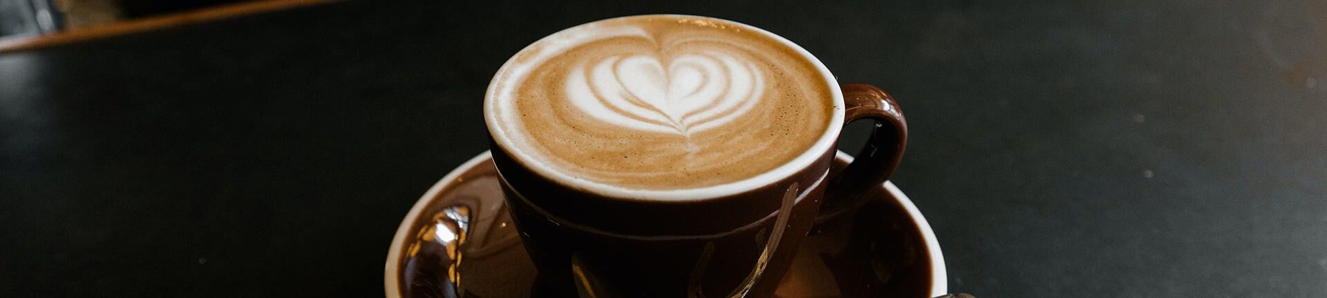 Eine Tasse Kaffee mit einem Herz Muster aus Milchschaum auf einem Tresen.