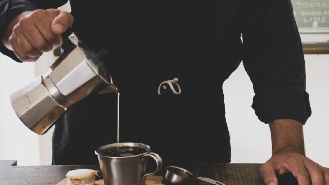 Mann schenkt Kaffee aus dem Espressokocher in eine Tasse