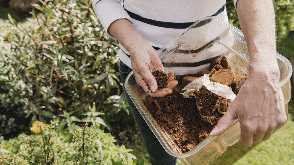 Frau im Garten hält Schale mit Kaffeesatz in der Hand