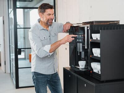 Mann bedient modernen Kaffeevollautomaten und bereitet frischen Kaffee in einem Büro zu.