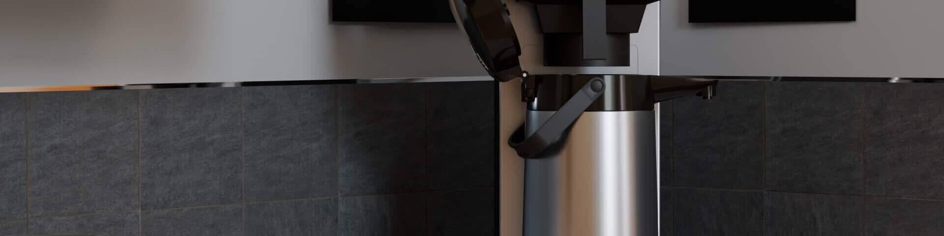 Filterkaffeemaschine auf einer Küchenarbeitsplatte, umgeben von grünen Schränken und schwarzer Fliesenrückwand.