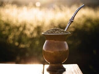 Mate-Becher mit Metallstrohhalm auf Holztisch bei Sonnenuntergang
