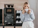 Frau-steht-mit-tasse-vor-kaffeebar-mit-barista-ultima