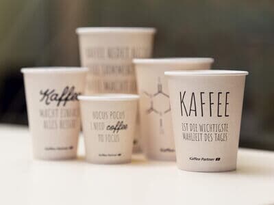 Kaffee Partner To Go Becher stehen nebeneinander auf dem Tisch