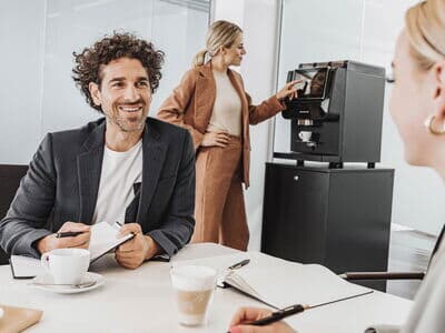 Mitarbeiter im Meeting, während jemand Kaffee an Maschine zieht