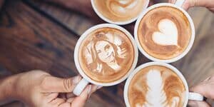 Vier Kaffeetassen mit Latte Art und einem Porträt im Schaum
