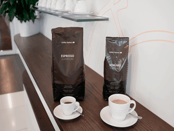 Zwei Kaffeepackungen von Kaffee Partner – Espresso Superiore und Schümli Gourmet – stehen nebeneinander auf einem dunklen Holztresen.