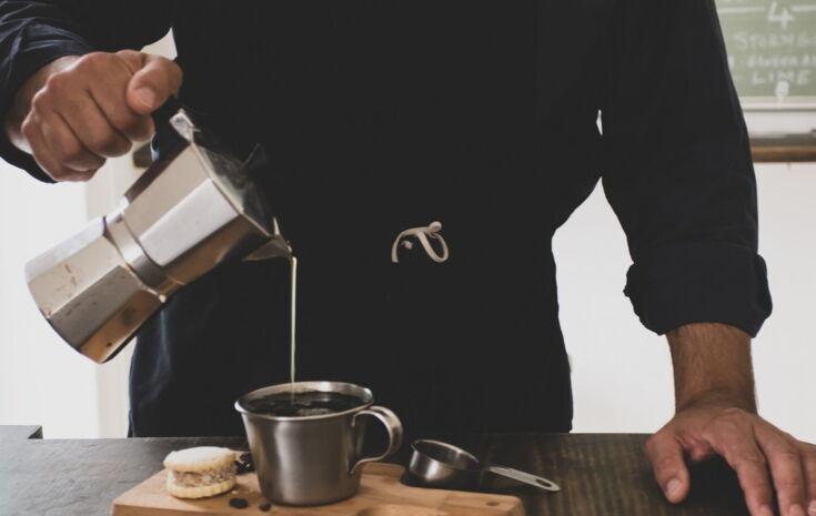 Mann schenkt Kaffee aus dem Espressokocher in eine Tasse