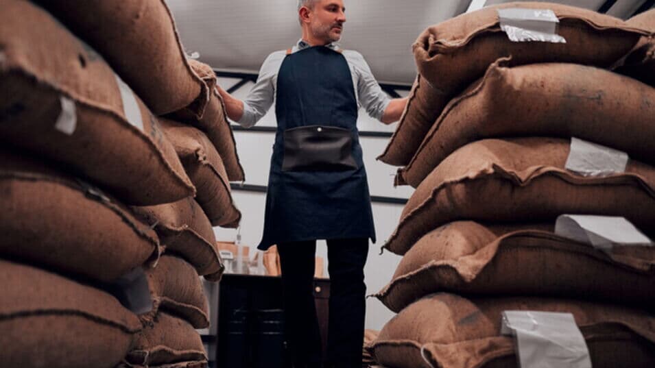Mann in Schürze steht in einem Lager für Kaffeebohnen