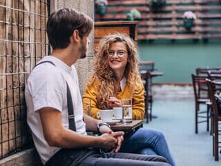 zwei personen sitzen draußen am tisch schauen sich an und trinken kaffee