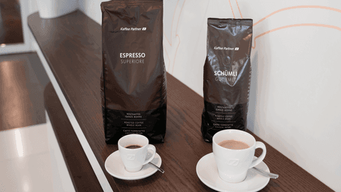 Zwei Kaffeepackungen von Kaffee Partner – Espresso Superiore und Schümli Gourmet – stehen nebeneinander auf einem dunklen Holztresen.