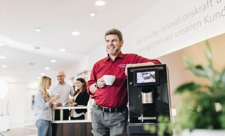 Service employee standing next to a coffee machine and drinking coffee.