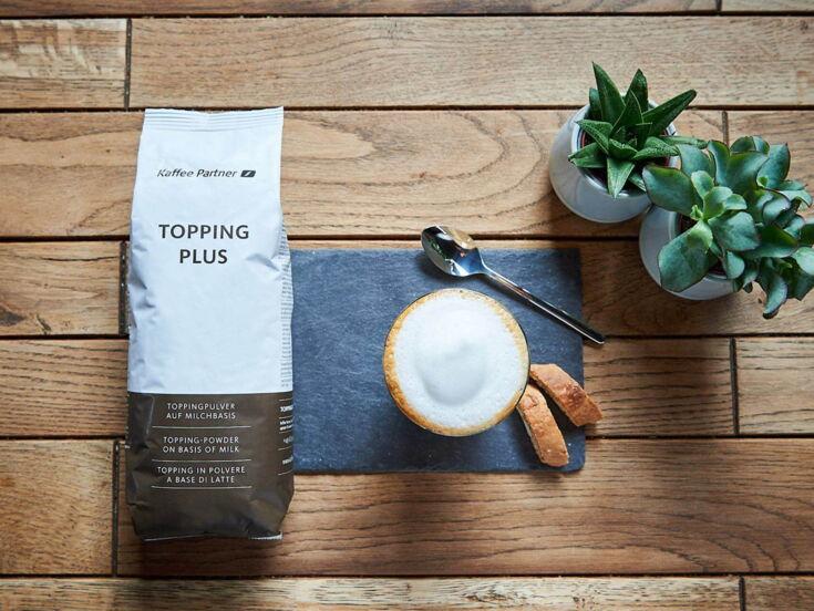 Eine Tüte Milchpulver Kaffee Partner Topping Plus liegt auf einem Holztisch