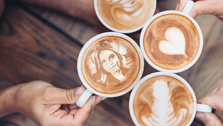 Vier Kaffeetassen mit Latte Art und einem Porträt im Schaum
