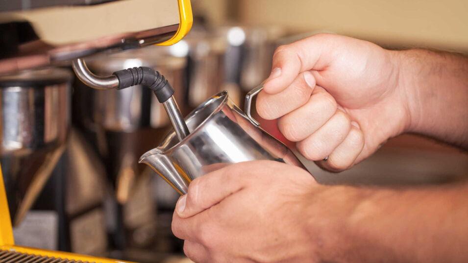Barista hält Milchkaennchen an eine Dampflanze