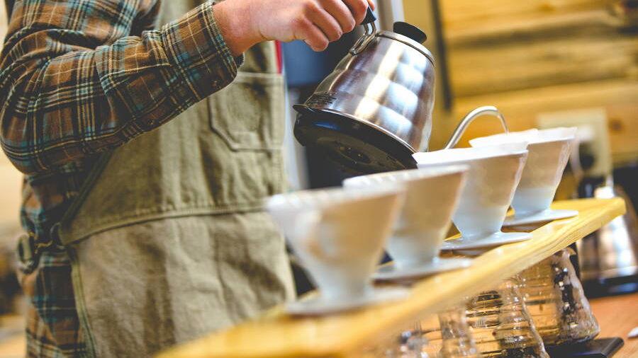 Ein Barista gießt heißes Wasser über eine Reihe Porzellan-Filter