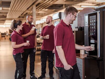 Vier Mitarbeitende trinken gemeinsam Kaffee und stehen an einer modernen Kaffeemaschine.