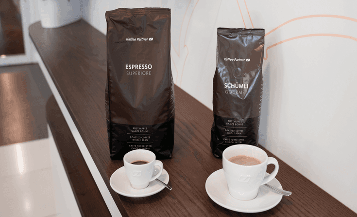 Zwei Kaffeepackungen von Kaffee Partner – Espresso Superiore und Schümli Gourmet – stehen nebeneinander auf einem dunklen Holztresen.