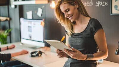 Eine lächelnde Frau steht im Büro mit einem Tablet in der Hand