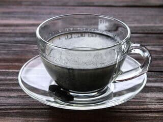 Schwarzer Goth Latte-Kaffee in einer Glastasse auf einem Holztisch