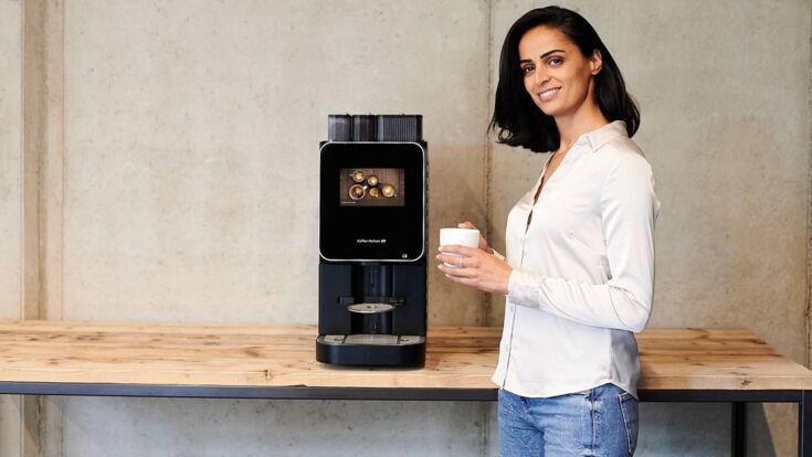 Frau steht neben der Barista Select mit einem Kaffee