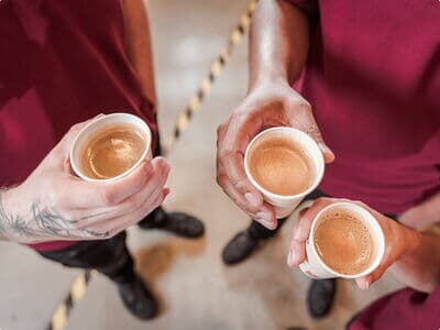 Drei Mitarbeiter halten Espressobecher während Kaffeepause in Produktion.