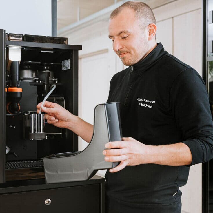 Techniker reinigt Teile eines geöffneten Kaffeevollautomaten im Büro