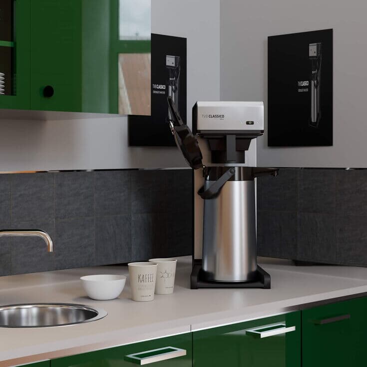 Filterkaffeemaschine auf einer Küchenarbeitsplatte, umgeben von grünen Schränken und schwarzer Fliesenrückwand.