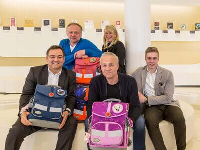 Mehrere Personen sitzen zusammen und halten Schulrucksäcke.