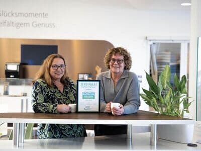 Zwei Personen zeigen ein Zertifikat für einen familienfreundlichen Arbeitgeber in moderner Büroumgebung.