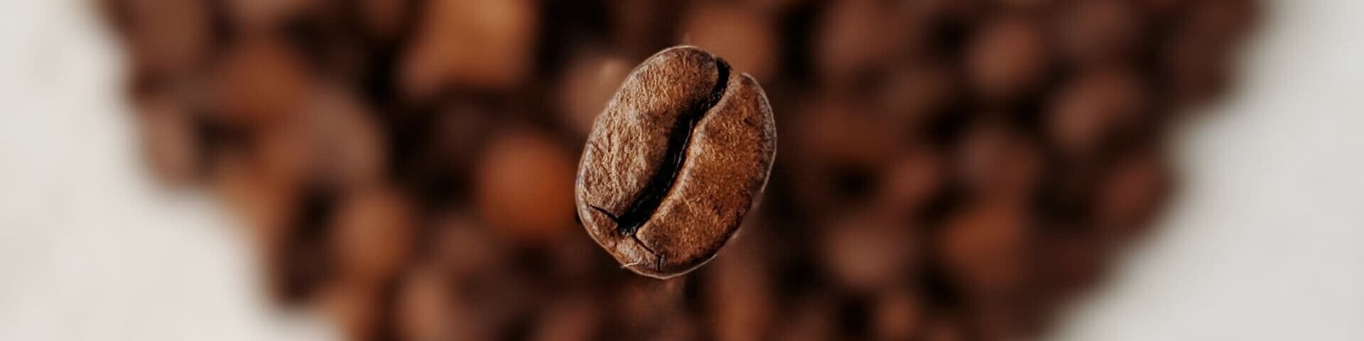 Geröstete Kaffeebohne schwebt über einem Herz aus Kaffeebohnen, die unscharf im Hintergrund erkennbar sind