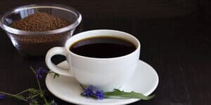 Weiße Tasse Zichorienkaffee mit Blüten und Schale Kaffeepulver