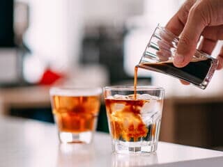 Espresso wird in Glas mit Eiswürfeln und Tonic Water eingeschenkt