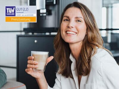 Lachende Frau mit Kaffee vor TÜV-Auszeichnung und Kaffeemaschine