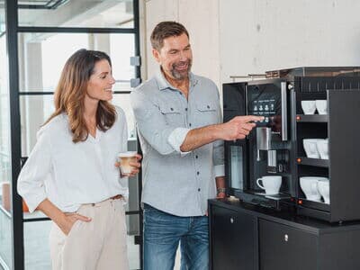 Zwei Personen nutzen einen Kaffeevollautomat im modernen Büro
