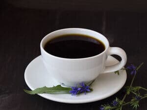 Weiße Tasse mit Zichorienkaffee und lila Blüten