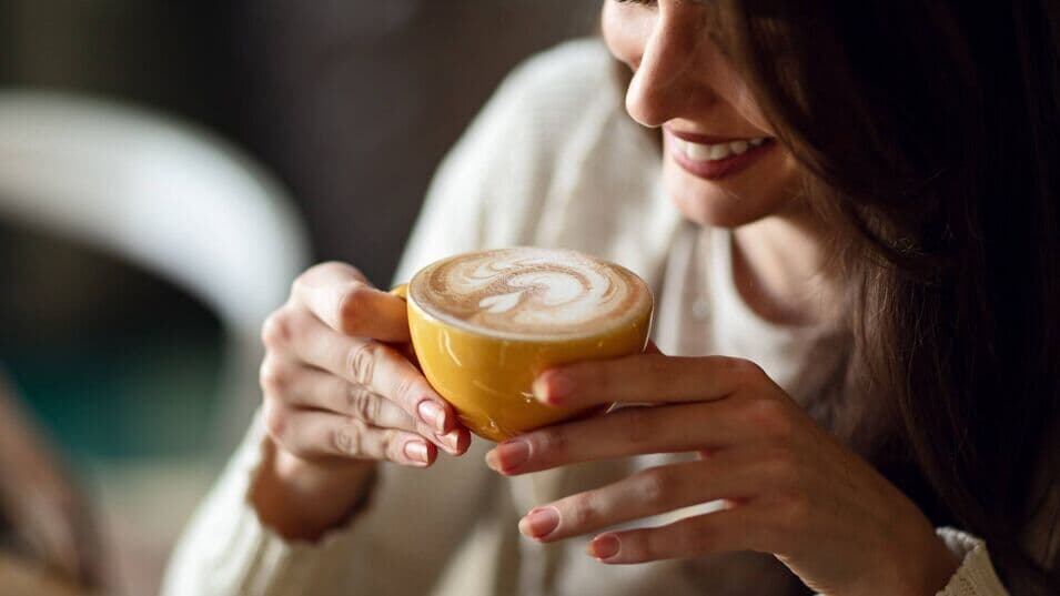 junge Frau trinkt Kaffee aus einer gelben Tasse