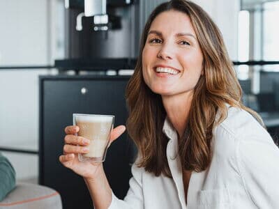 Lachende Frau hält Glas Latte Macchiato in der Hand