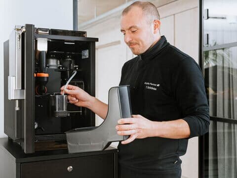 Techniker reinigt Teile eines geöffneten Kaffeevollautomaten im Büro