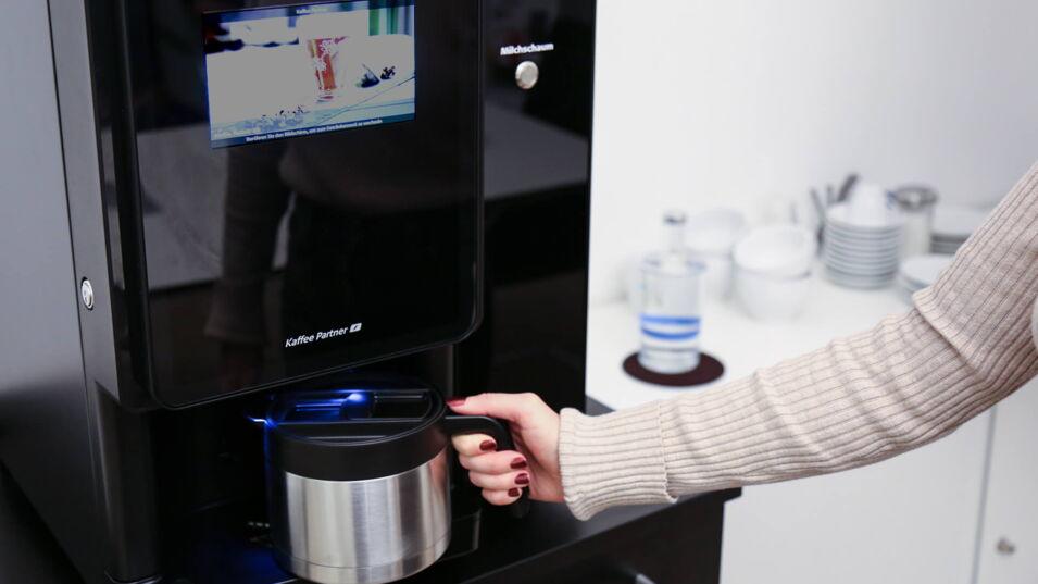 Frau stellt Kanne unter Kaffeeautomaten