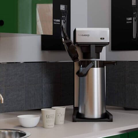 Filterkaffeemaschine auf einer Küchenarbeitsplatte, umgeben von grünen Schränken und schwarzer Fliesenrückwand.