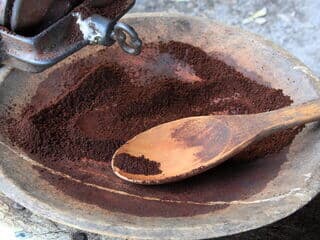 Holzlöffel mit frisch gemahlenem Kaffee in rustikaler Schale neben Kaffeemühle.