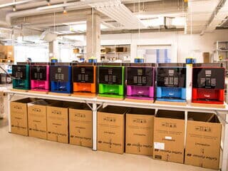 Kaffeevollautomaten in Türkis, Pink, dunkel blau, orange, grün, lila, hell blau und rot stehen verpackungsbereit auf Tischen