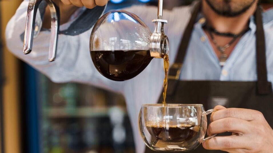 Barista schenkt fertig gebrühten Kaffee aus dem Syphon in eine Tasse ein