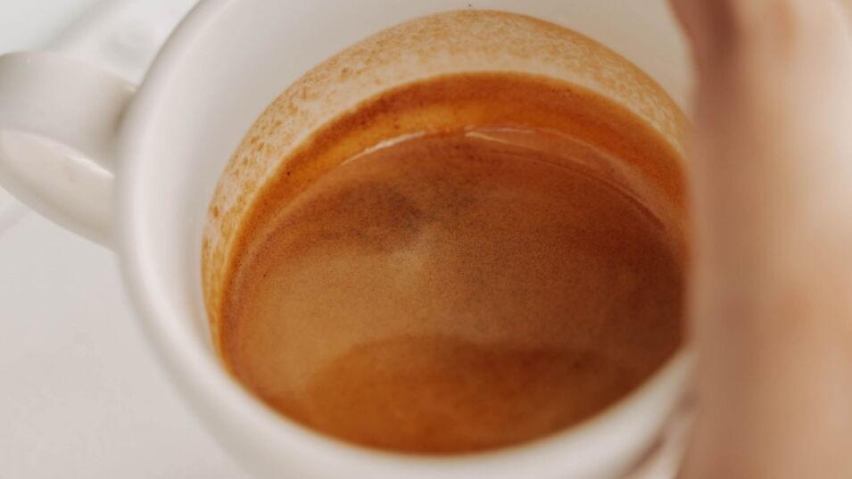 Eine Hand hält eine Tasse Kaffee Crema, dabei ist der Fokus auf der Crema