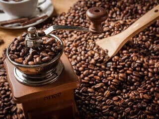 Handkaffeemühle voller Bohnen neben Holzlöffel auf Kaffeebohnen.