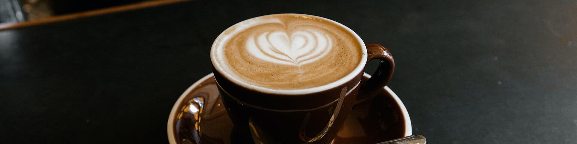 Eine Tasse Kaffee mit einem Herz Muster aus Milchschaum auf einem Tresen.