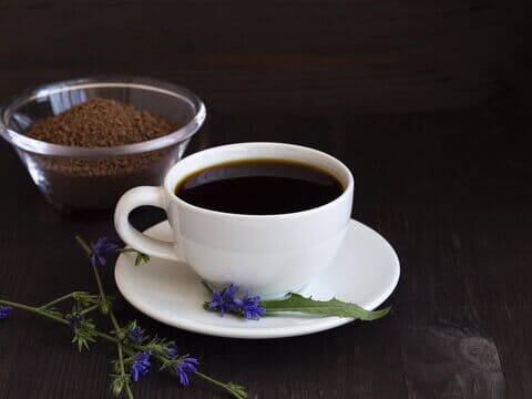 Weiße Tasse Zichorienkaffee mit Blüten und Schale Kaffeepulver